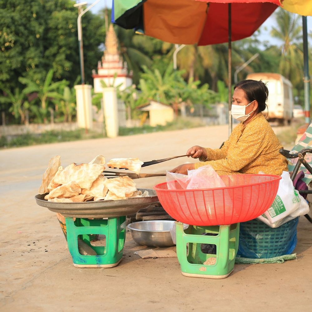 Roadside vendor frying snacks beside a temple in rural Cambodia