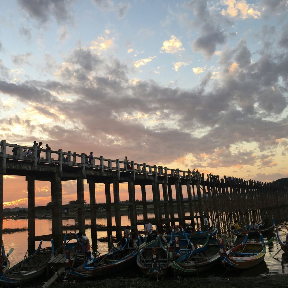 The wooden U Bein Bridge silhouetted at sunset over the water
