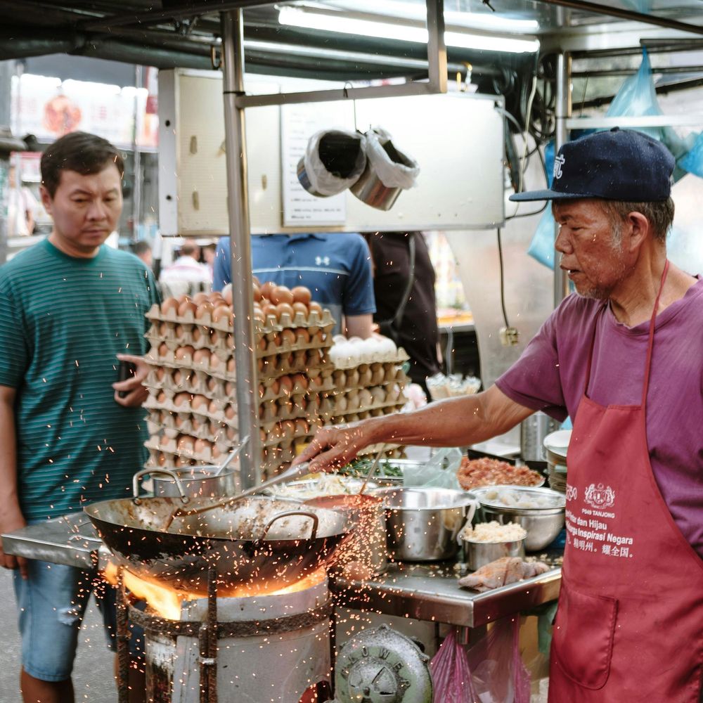 Street food hawker cooking over an open flame at a local market stall