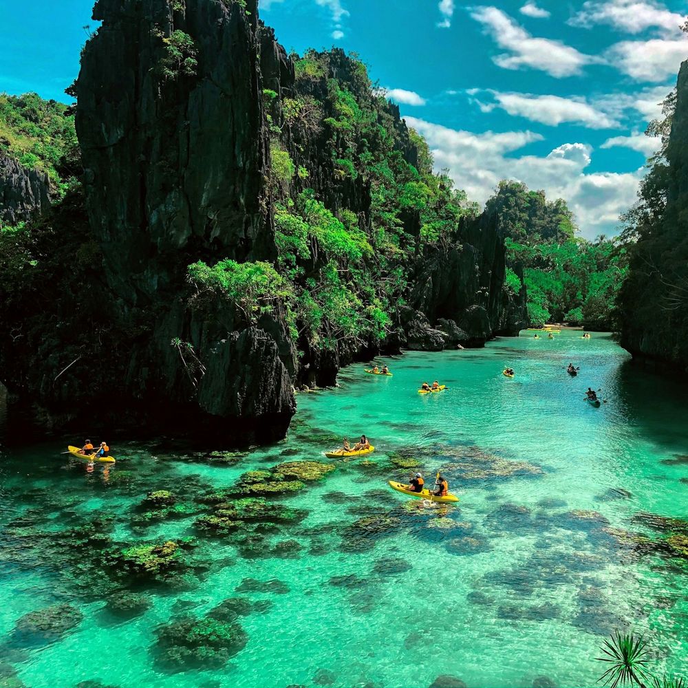 Kayakers in the clear turquoise lagoon of El Nido, Palawan, surrounded by limestone cliffs