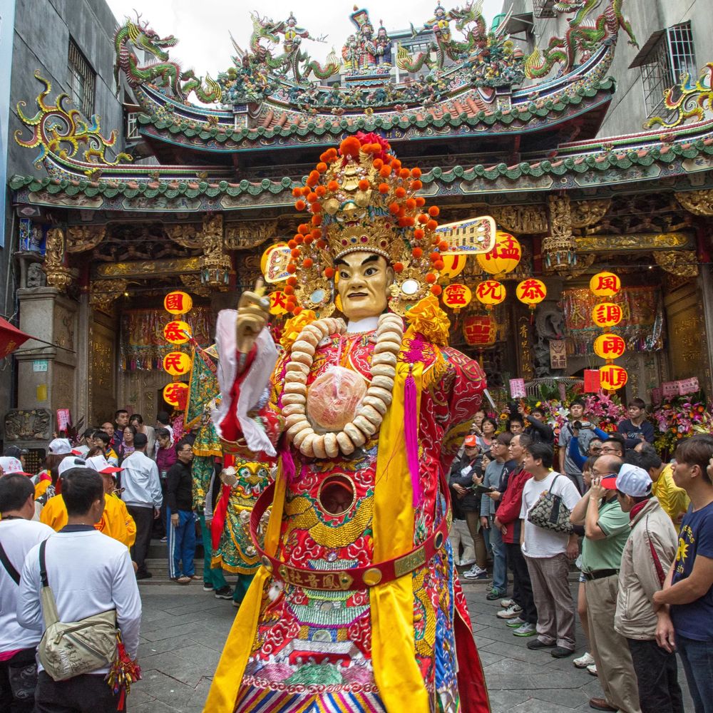 Costumed performer in a religious temple procession surrounded by crowds