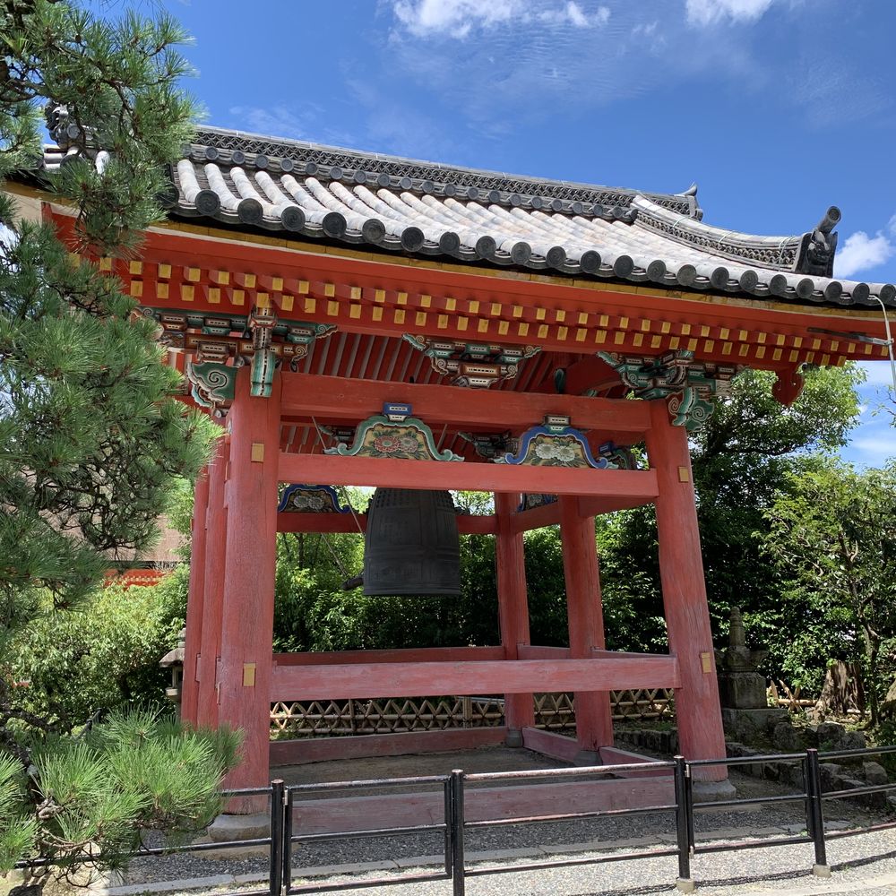 Red wooden bell tower at a Buddhist temple amid pine trees